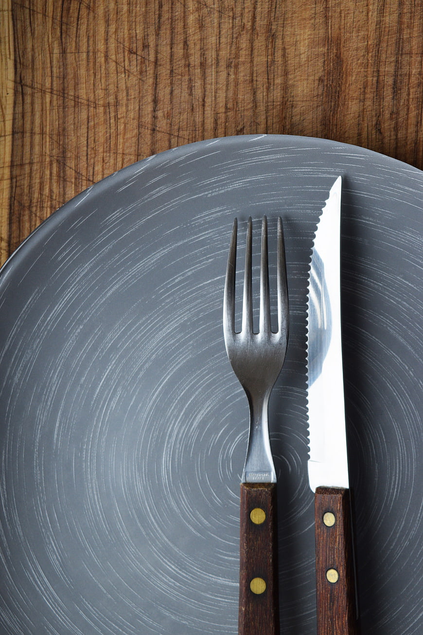 Top view of fork and knife on gray plate with wooden background