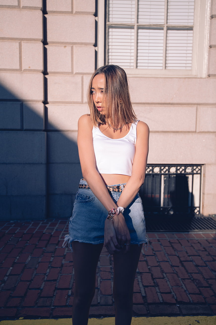 Young woman in white crop top and denim skirt standing on brick sidewalk