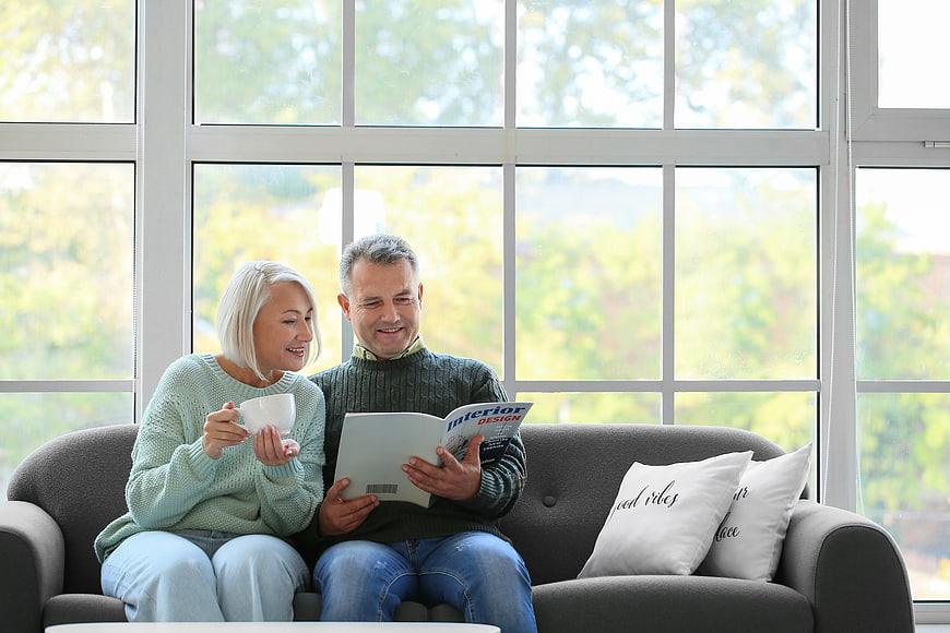 Happy senior couple reading interior design magazine on sofa