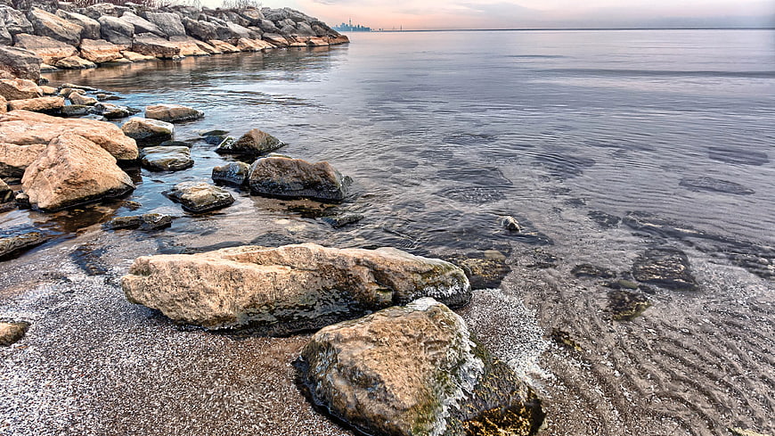 Rocky shoreline with clear water and distant city skyline