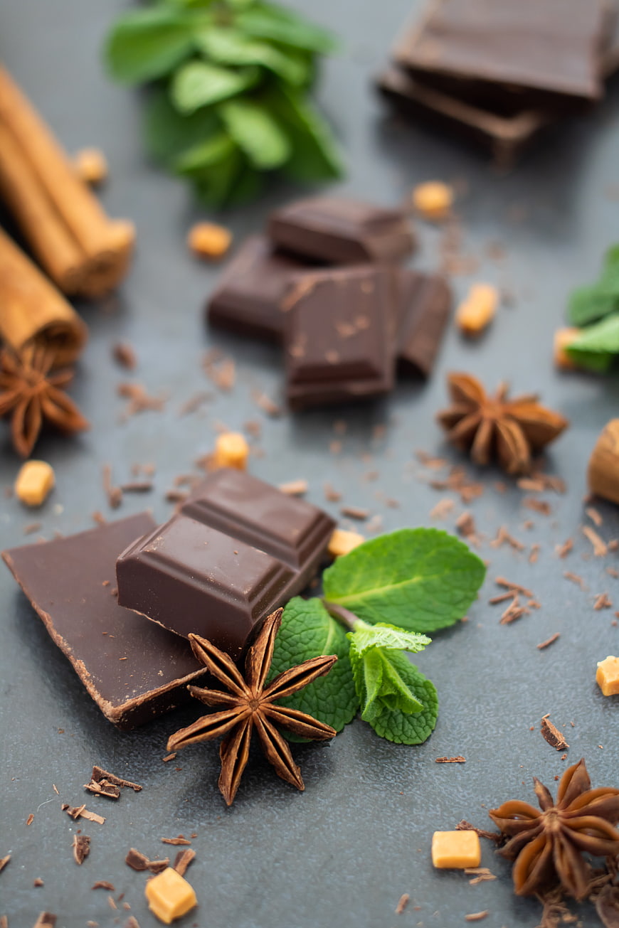 Dark chocolate pieces with mint leaves and star anise on dark background