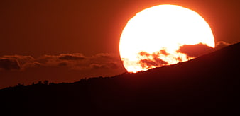 Giant Orange Sun Setting Behind Silhouetted Mountain Ridge