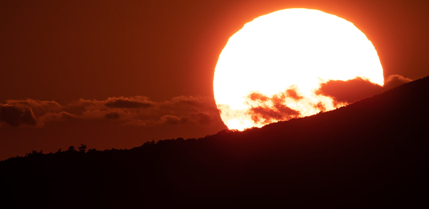 Giant Orange Sun Setting Behind Silhouetted Mountain Ridge
