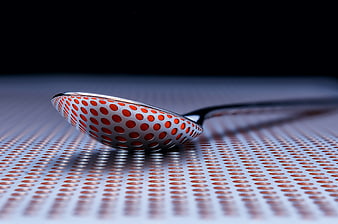 Abstract metal spoon with orange dots on perforated surface