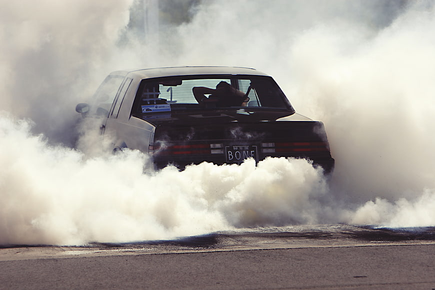 White car performing burnout with thick smoke on asphalt