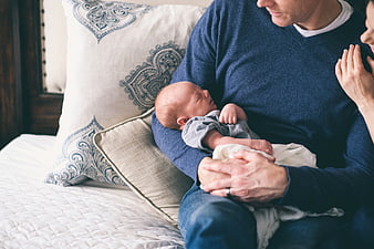 Parents holding sleeping newborn baby on bed