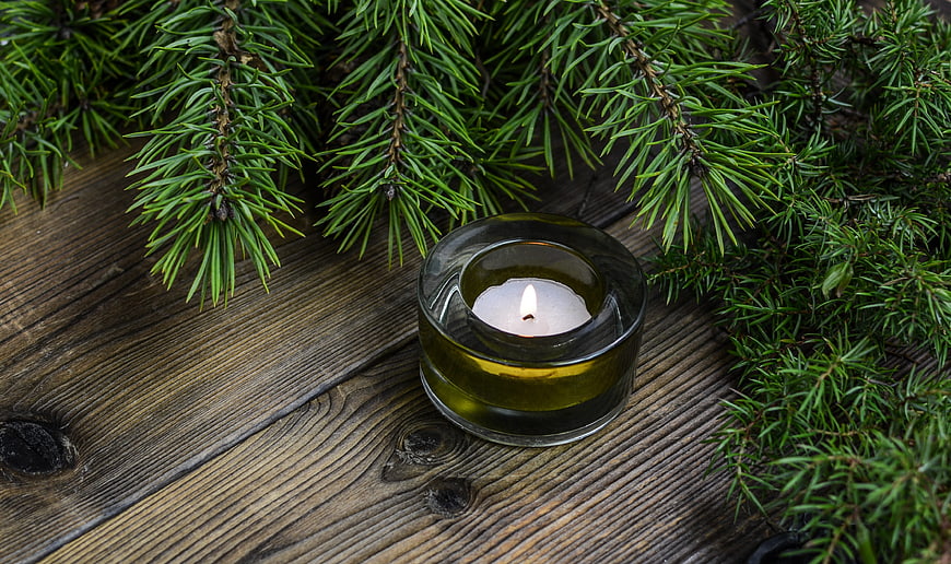 Lit tealight candle in green glass holder with pine branches on wood