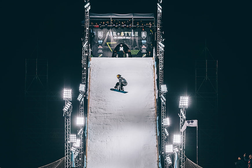 Snowboarder performing aerial trick on night slope at Air + Style event