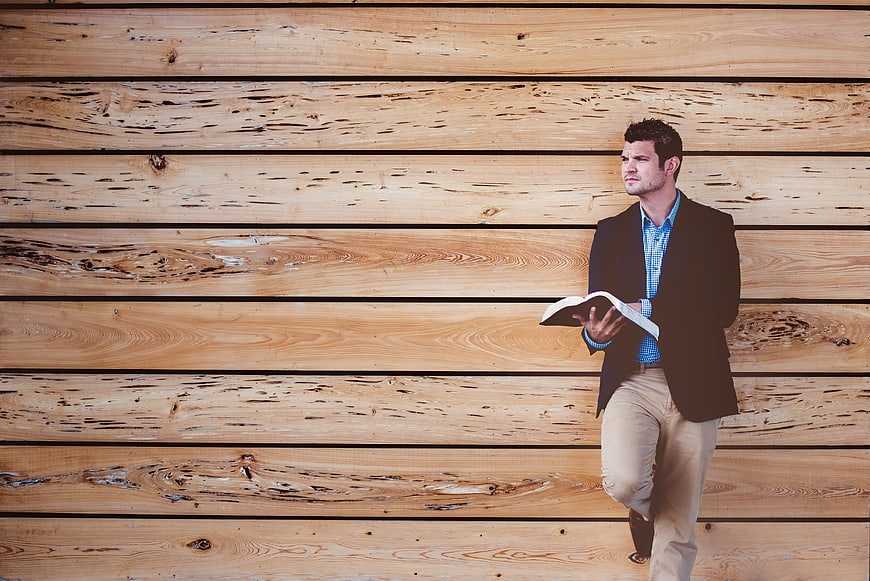 Man in blazer reading book against wooden wall background