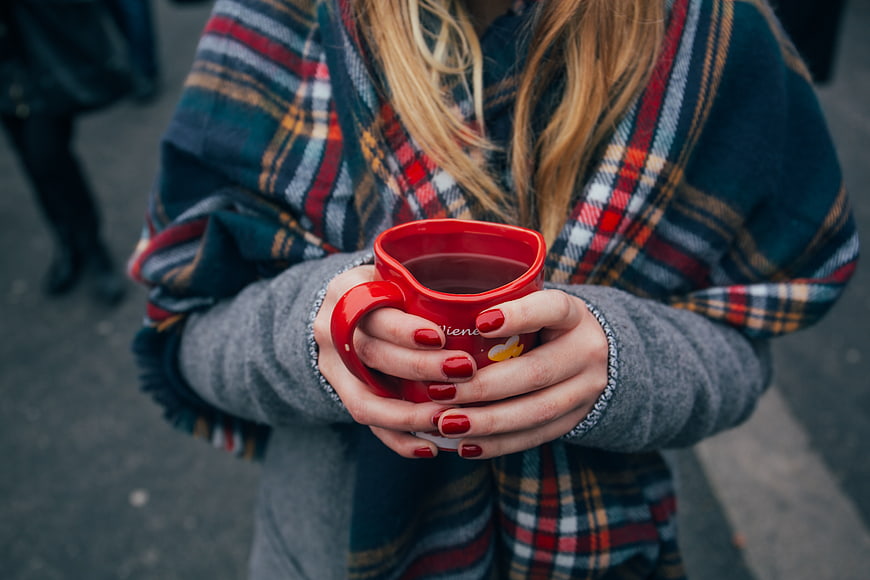 Woman holding red coffee mug in plaid shawl