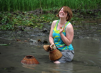 Woman kneeling in muddy rice paddy holding fish in basket