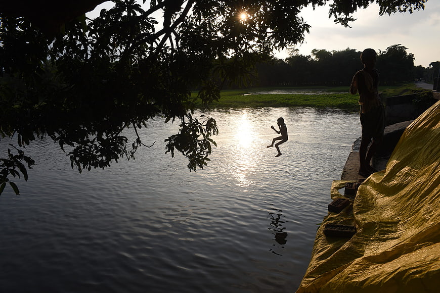 Silhouette of child jumping into river at sunset