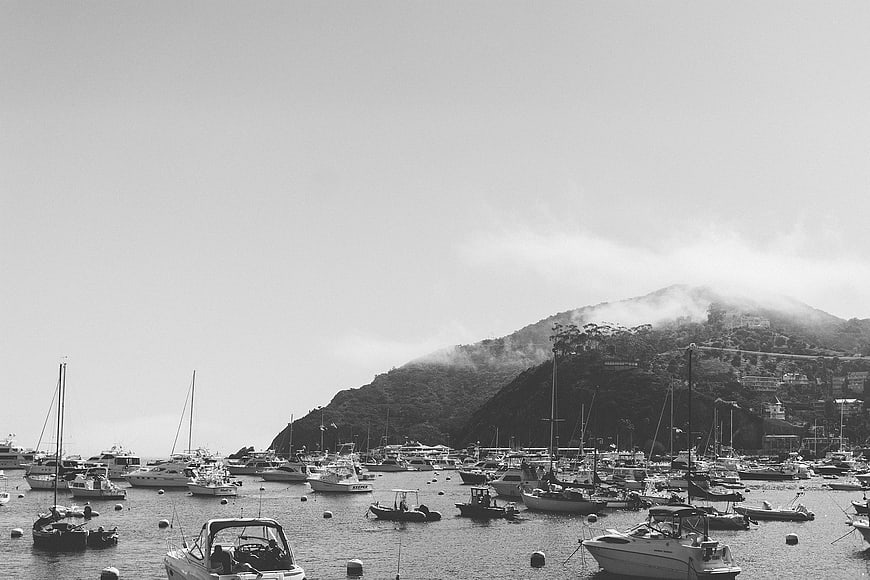 Black and white harbor scene with boats and misty mountain