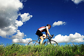 Cyclist Riding Road Bike On Grassy Hill Under Blue Sky