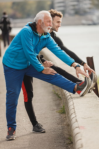 Senior and young man stretching legs outdoors by river