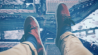 POV of red sneakers dangling over snowy city skyline from skyscraper edge
