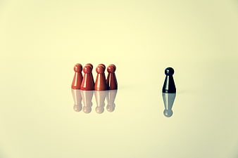 Black game piece standing apart from red group on beige background