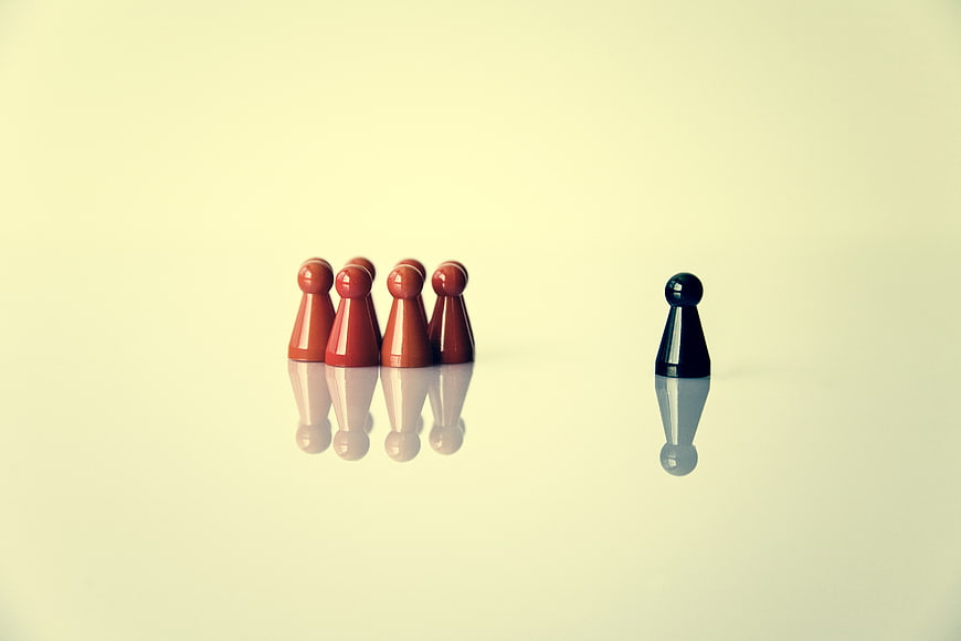Black game piece standing apart from red group on beige background