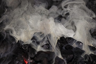 Close-up of white smoke rising from hot black coal embers