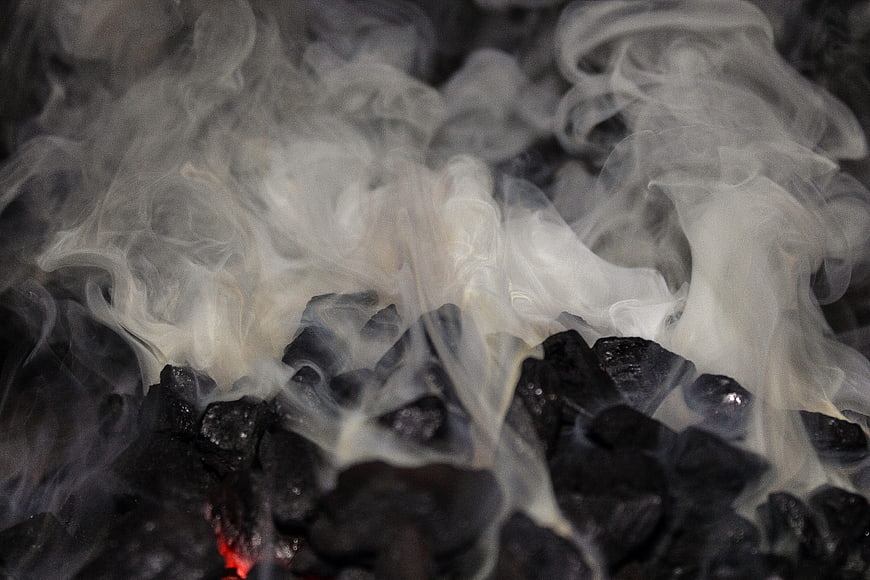 Close-up of white smoke rising from hot black coal embers