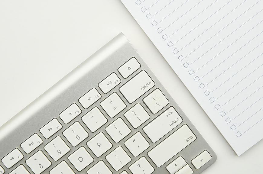 Minimalist silver keyboard and blank checklist paper on white desk