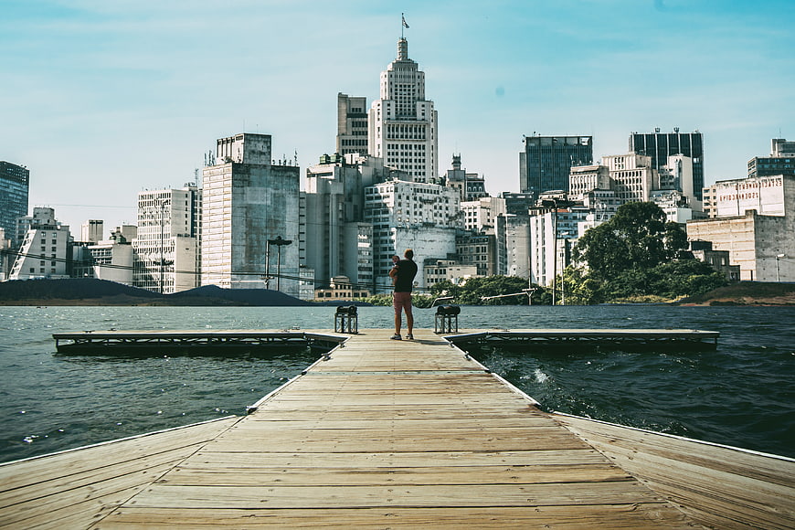 Man standing on wooden pier looking at city skyline