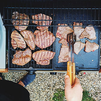 Top view of pork steaks grilling on barbecue with tongs