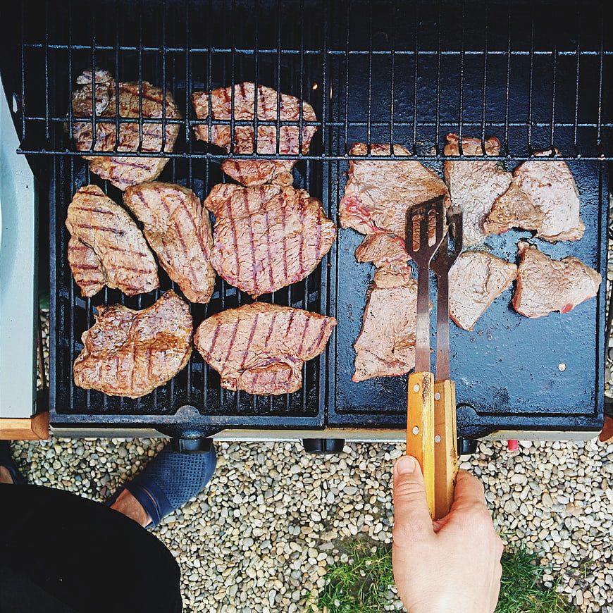 Top view of pork steaks grilling on barbecue with tongs
