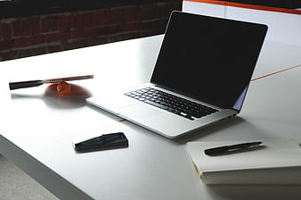 Modern workspace with laptop, smartphone, and notepad on white desk