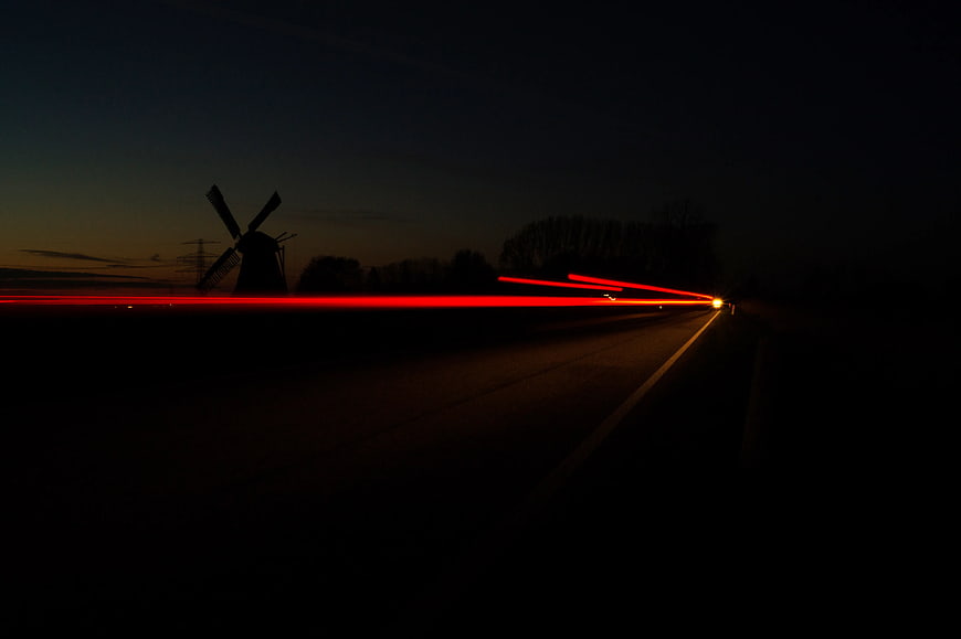 Long Exposure Red Taillight Trails on Dark Road with Windmill