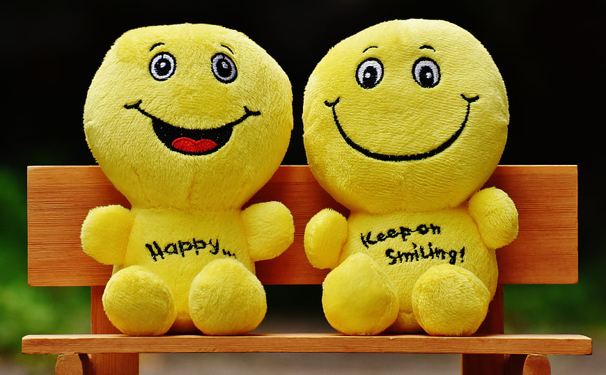 Two yellow smiley plush toys sitting on a wooden bench