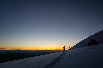 Silhouetted Skiers on Snowy Mountain Ridge at Sunset