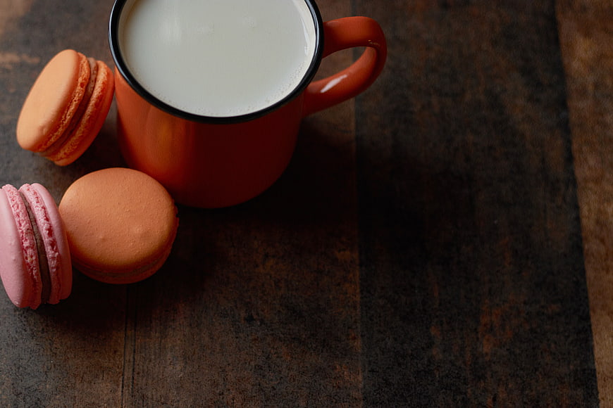Orange mug of milk with macarons on rustic wood