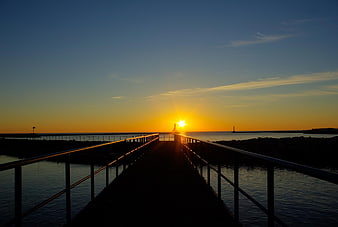 Silhouette of pier walkway leading to sunrise over calm ocean