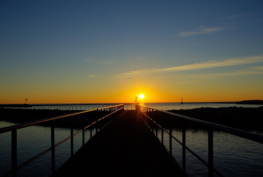 Silhouette of pier walkway leading to sunrise over calm ocean