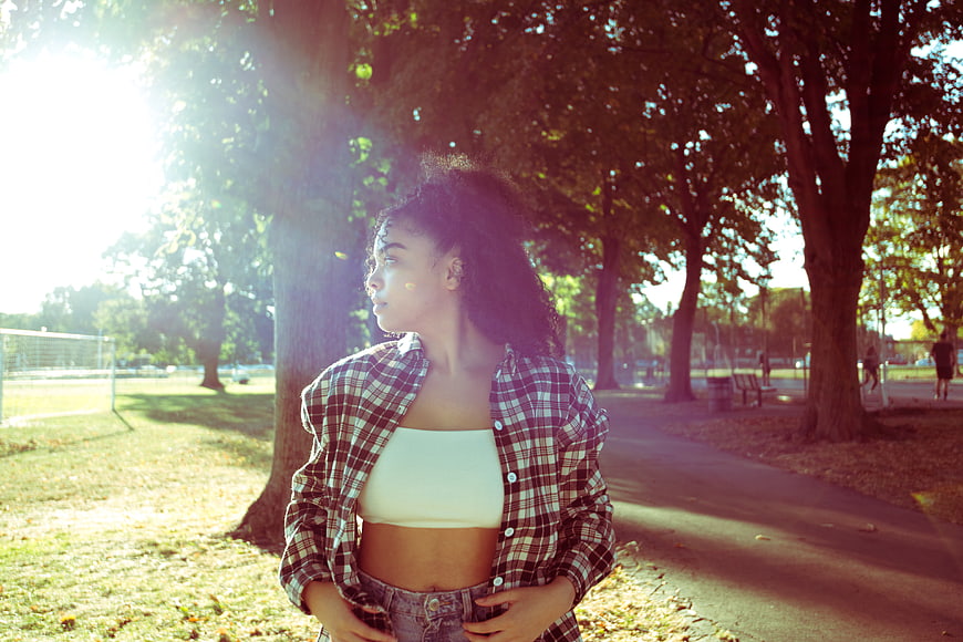 Young woman in plaid shirt standing in park with sun flare