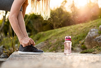 Woman tying running shoe with water bottle outdoors