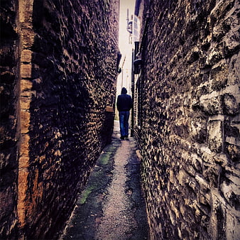 Man in Hoodie Walking Down Narrow Stone Alleyway