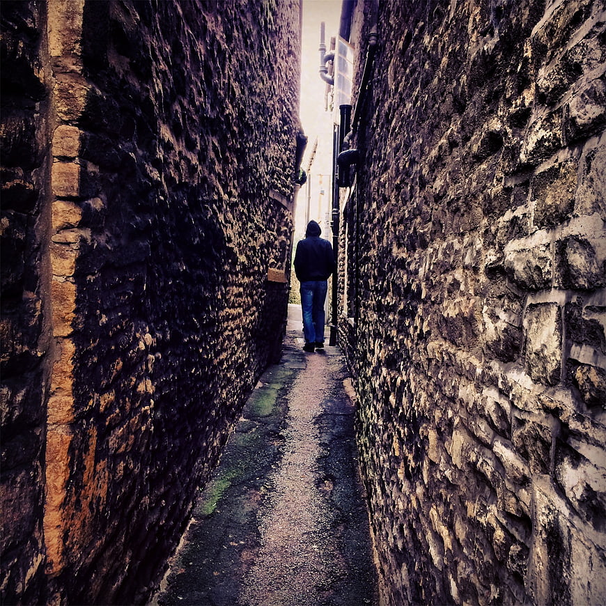Man in Hoodie Walking Down Narrow Stone Alleyway