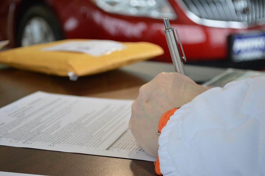 Hand Signing Car Purchase Contract with Red Vehicle Background