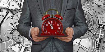 Businessman holding red alarm clock against clock background
