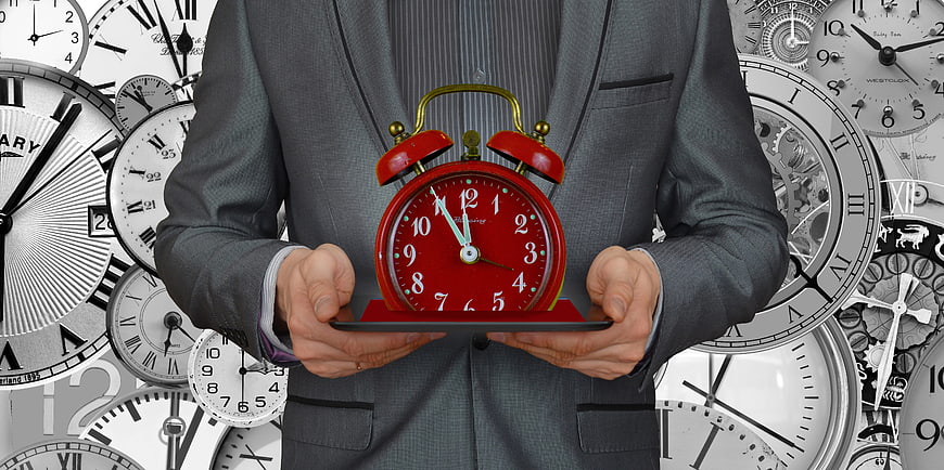 Businessman holding red alarm clock against clock background