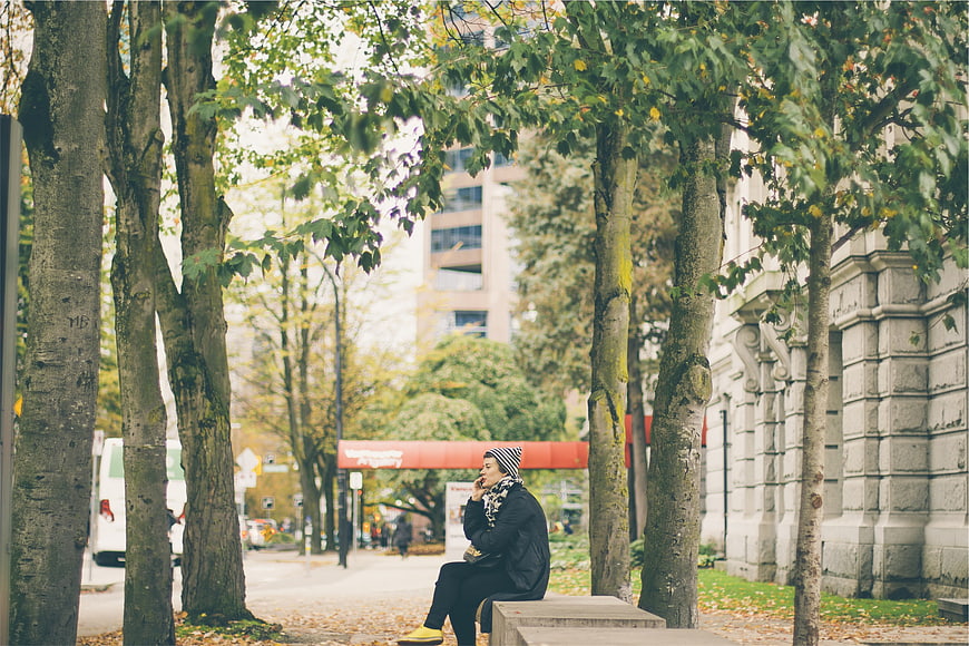 Woman sitting on bench talking on phone in autumn city park