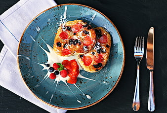 Overhead view of berry pancakes with cream on blue plate