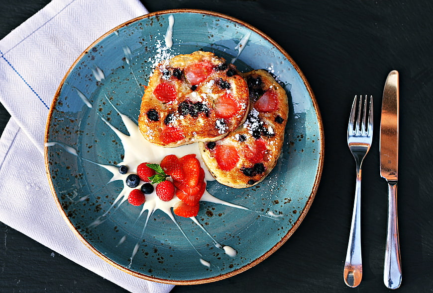 Overhead view of berry pancakes with cream on blue plate
