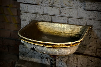 Rusty vintage metal sink mounted on white brick wall