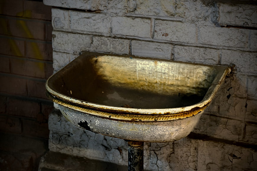 Rusty vintage metal sink mounted on white brick wall