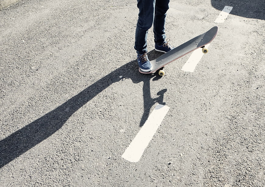 Skateboarder Feet on Asphalt Road with Long Shadow