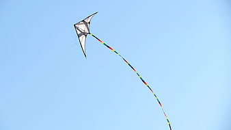 White stunt kite with rainbow tail flying in blue sky