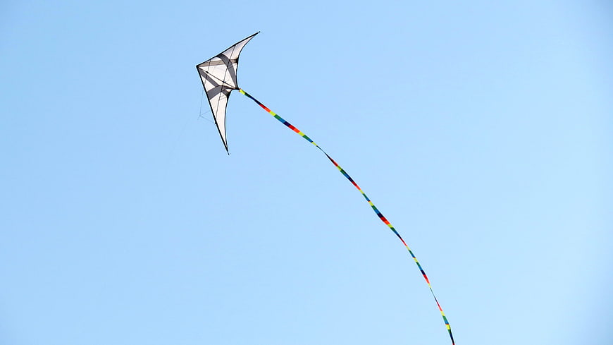 White stunt kite with rainbow tail flying in blue sky